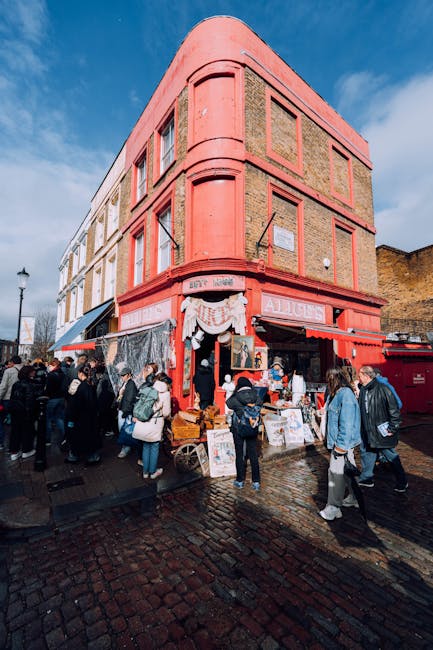 A busy street scene outside a brick building with a red and green striped awning, on the facade of which is a sign reading 'ANTIQUES'. Several pedestrians, including men and women dressed casually, wa